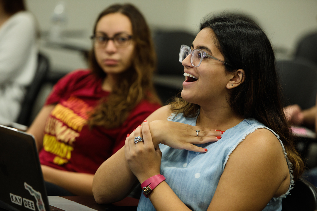 A student sitting at a classroom desk talking and smiling