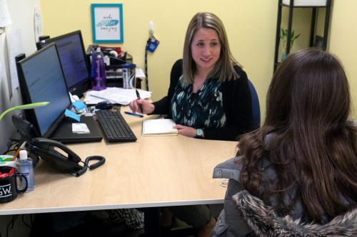 A student and an advisor sit across a desk from each other looking at a computer